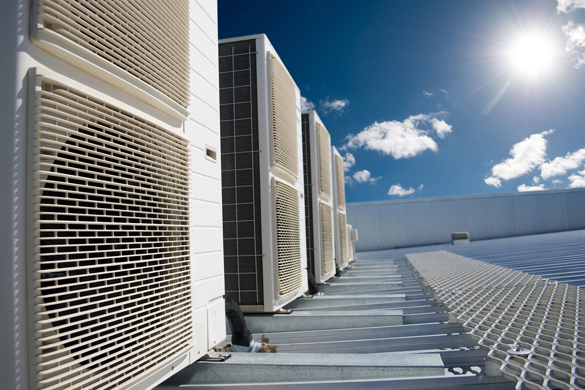 Air conditioner units on a roof of industrial building with blue sky and clouds in the background.